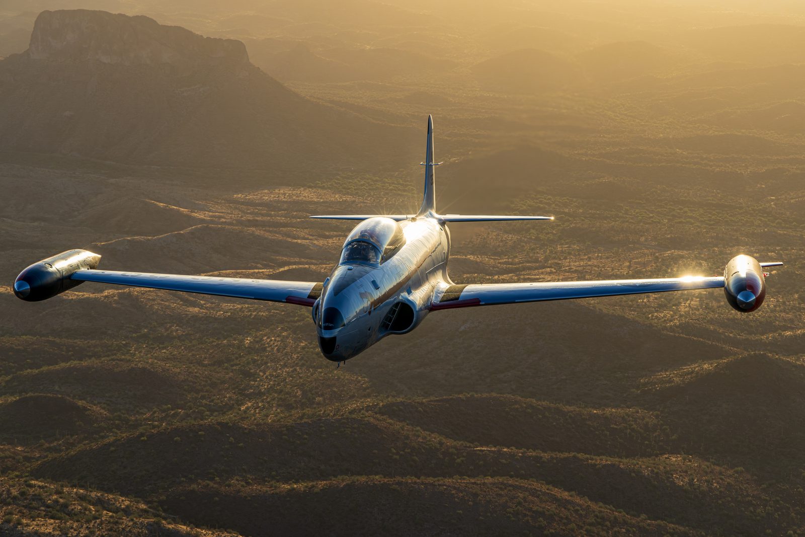 Silver Canadair CT-133 Silver Star jet trainer banking in low evening sunlight above the Superstition Mountains.
