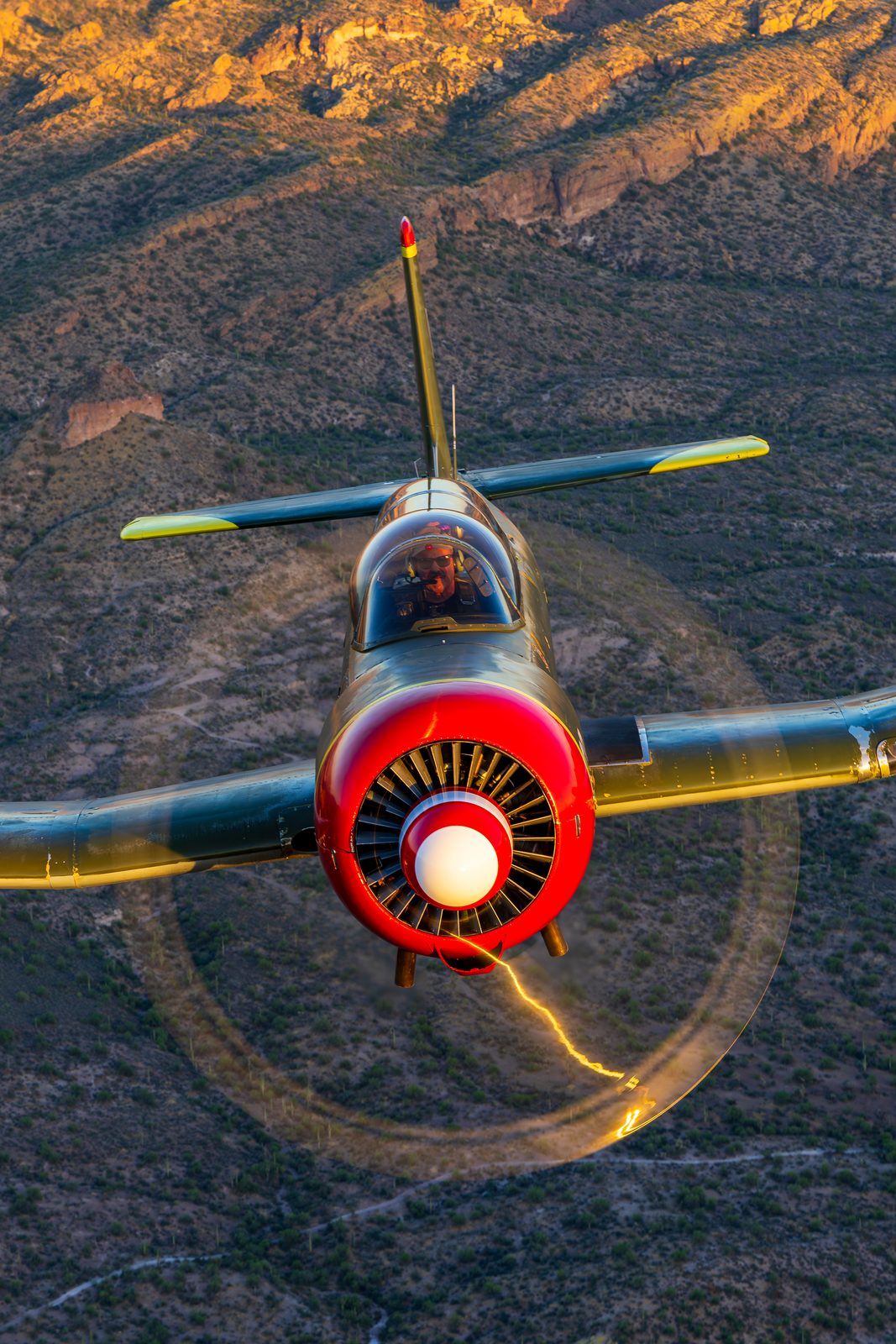 Head-on view of a Nanchang CJ-6A trainer, propeller blurred into a disc, against desert hills.
