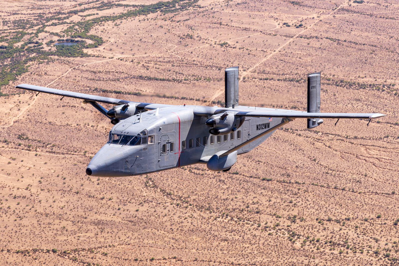 Twin-engined Short C-23B Sherpa flying above dry desert terrain seen from above.